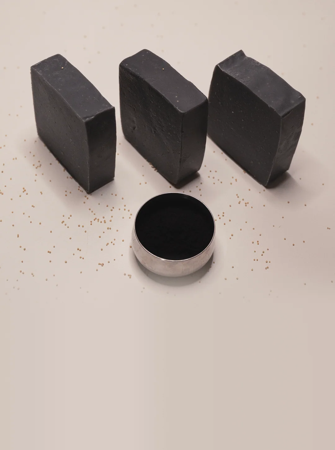 Three bars of Noir charcoal soap standing in a row, a small tin of charcoal powder in front