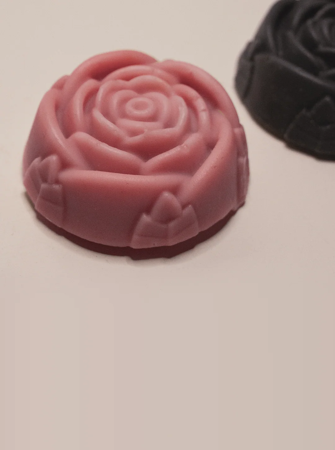 A pink rose-moulded soap between two charcoal rose soaps