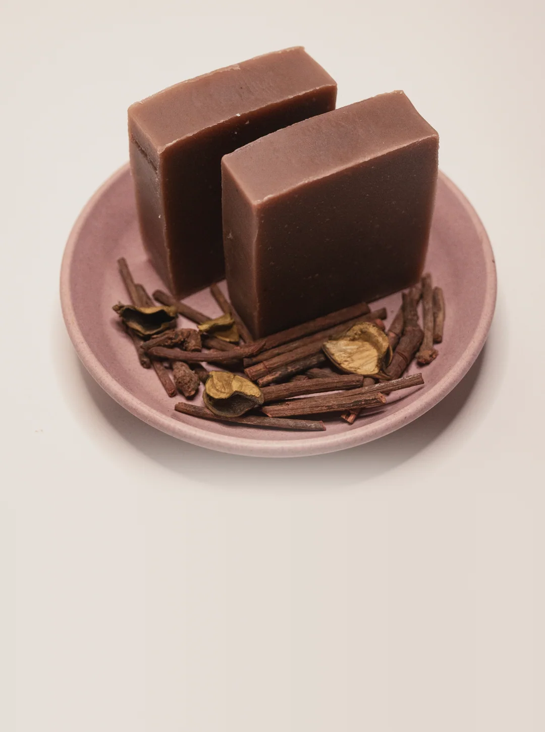 Two bars of Ruby Root manjistha soap on a pink dish with dried madder root