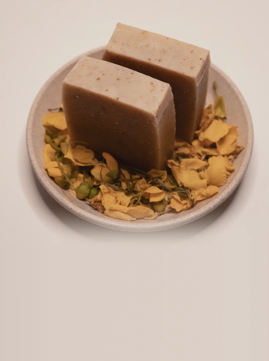 Two bars of tangedu tanner's cassia soap on a stone dish strewn with dried cassia flowers