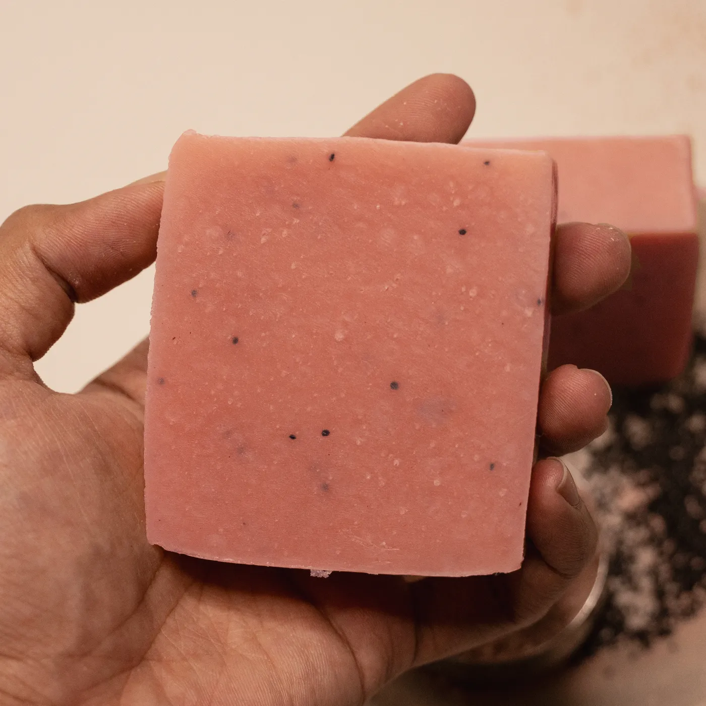 A bar of Paris pink clay soap held in a hand, poppy seed flecked through it